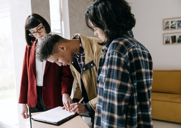 A landlord overseeing two tenants signing their lease agreement